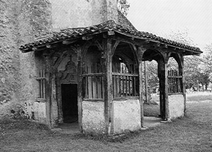 En avant de la façade occidentale qui forme clocher-mur, un porche grâcieux fait de bois et de maçonnerie abrite un portail du XVe ou XVIe siècle (photo 1980, églises anciennes du Gabardan). - Lubbon